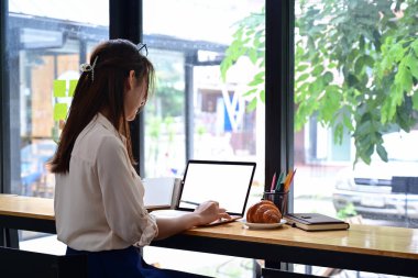 Kafede oturan ve dizüstü bilgisayar kullanan genç bir kadın..