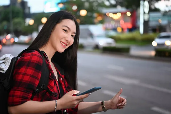 城市里兴高采烈的年轻女性晚上在智能手机上使用出租车服务应用程序 — 图库照片