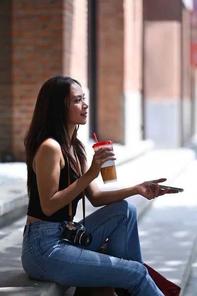 年轻女子坐在户外喝咖啡和使用智能手机的肖像 — 图库照片