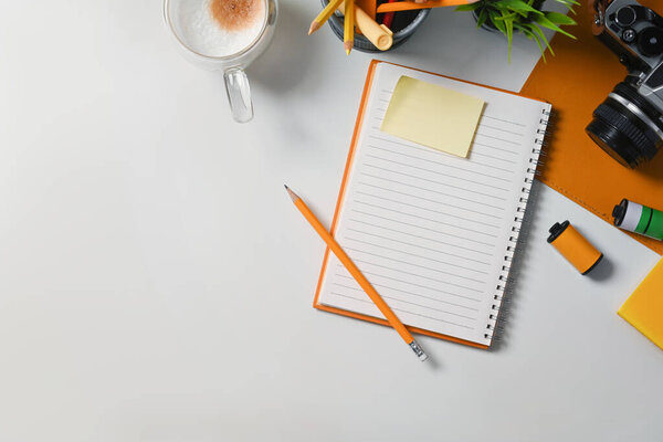 Above view empty notebook, sticky note, coffee cup and camera on white table.