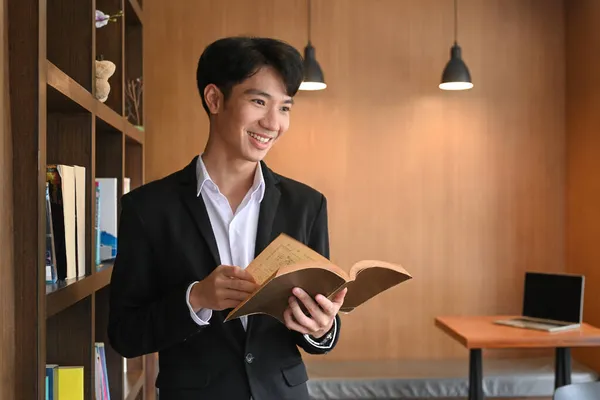 Χαμογελώντας Επιχειρηματίας Κρατώντας Βιβλίο Και Στέκεται Στο Σύγχρονο Χώρο Εργασίας — Φωτογραφία Αρχείου