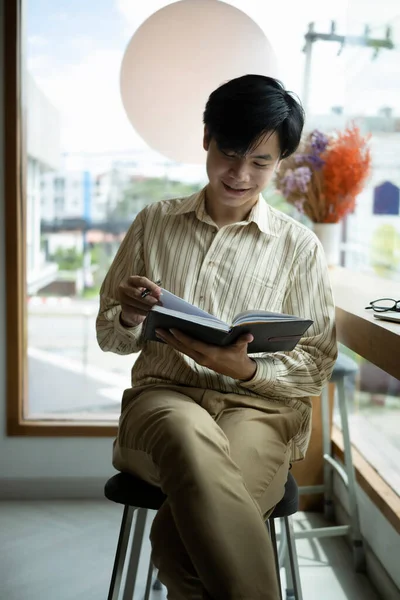 Улыбающийся Молодой Азиат Сидит Светлом Офисе Читает Книгу — стоковое фото
