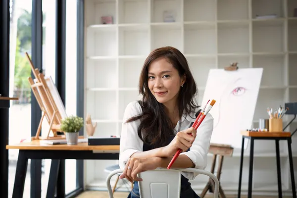 笑顔の女性アーティストが絵筆を持ち 彼女のアートスタジオに座って — ストック写真