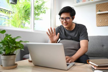 Mutlu Asyalı adamın oturma odasındaki dizüstü bilgisayarda görüntüsü var..