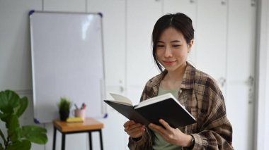 Modern işyerinde otururken kitap okuyan düşünceli genç bir kadın..