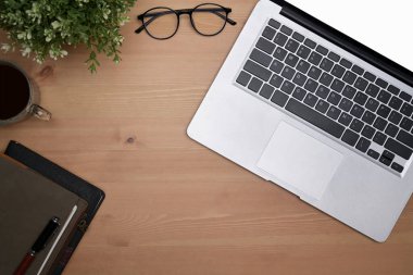 Diz üstü bilgisayar, gözlük, kahve fincanı ve tahta arka planda not defteri..