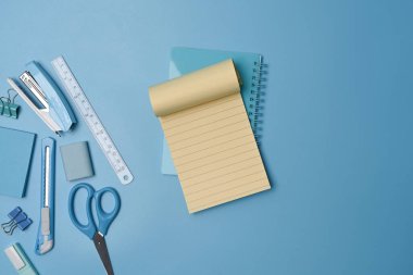 Boş defter ve mavi arka planda çeşitli kırtasiye malzemeleri. Okul konseptine dönelim..