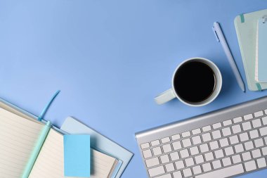 Üst görünüm kahve fincanı, klavye ve mavi arkaplanda not defteri..