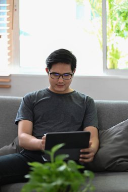 Kanepede oturan yakışıklı adam ve bilgisayar tabletiyle internette geziniyor..