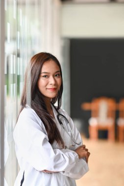 Beyaz üniformalı güzel bayan doktor kollarını kavuşturup kameraya gülümsüyor..