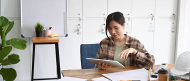 Gülümseyen genç bayan mimar iş yerinde dijital tabletle proje üzerinde çalışıyor..