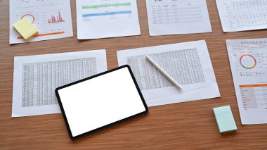 Sayısal tablet ve finansal dökümanlar ahşap masanın üzerinde.