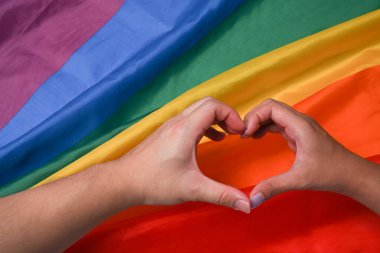 Kadın homoseksüel çift LGBT gökkuşağı bayrağına el kalp işareti yapıyor..