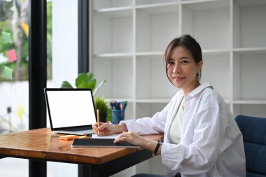 Genç bayan girişimci modern iş yerinde oturuyor ve kameraya gülümsüyor..