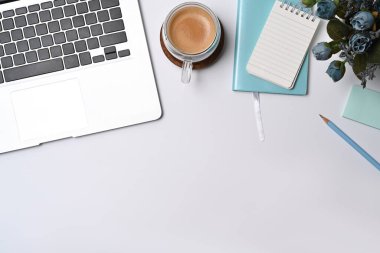 Dizüstü bilgisayar, not defteri ve kahve fincanı beyaz ofis masasında..