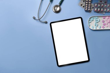 Dijital tablet, steteskop ve mavi arka planda renkli tıbbi haplar..