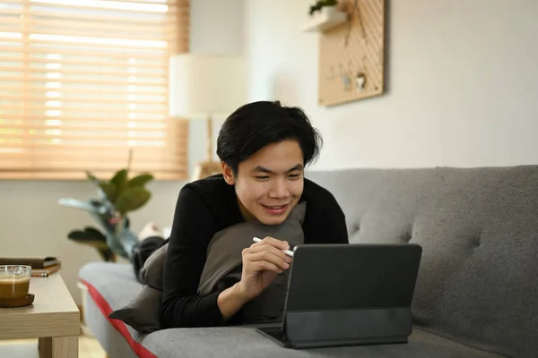 Mosolygó Ázsiai Férfi Használ Számítógép Tabletta Kanapén Otthon — Stock Fotó