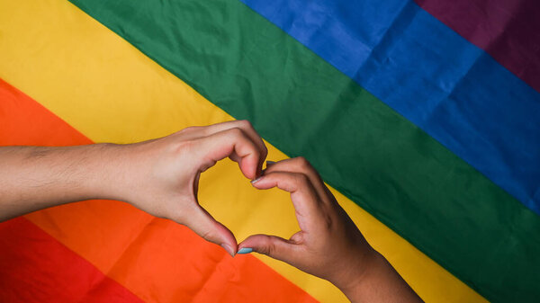 Женская гомосексуальная пара делает знак руки на фоне радужного флага..