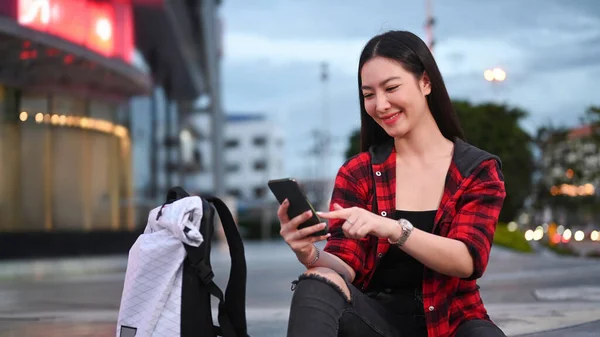 晚上坐在城市楼梯上用智能手机笑着的亚洲女人 — 图库照片