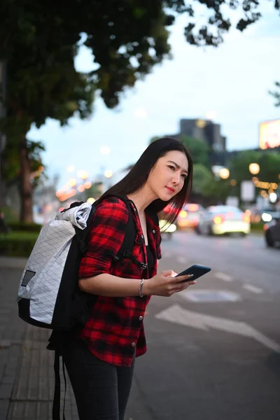 年轻的亚洲女人站在路边 手里拿着智能手机等出租车 — 图库照片