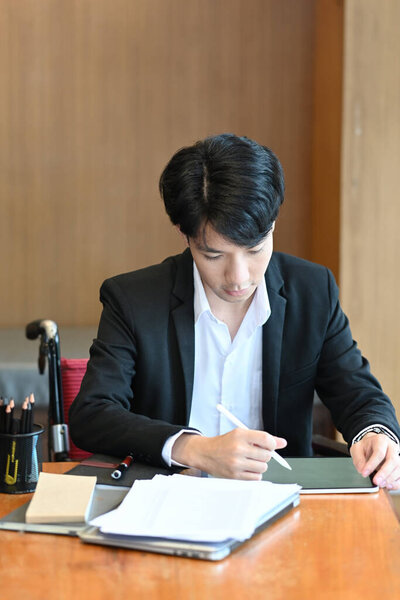 Инвалид в инвалидной коляске работает с цифровым планшетом в офисе.