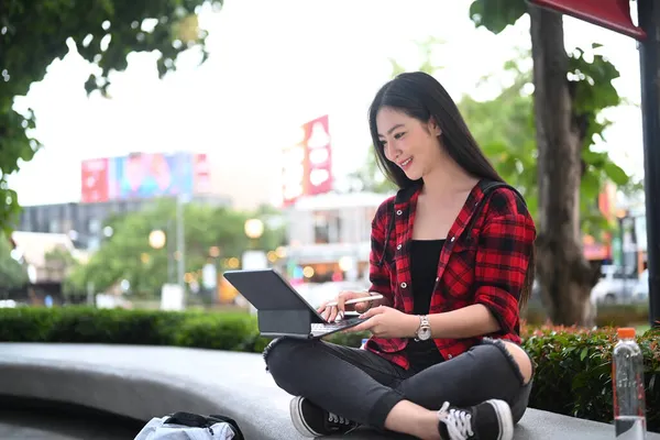 年轻的亚洲女人坐在城市公园的长椅上 用数码平板电脑 — 图库照片