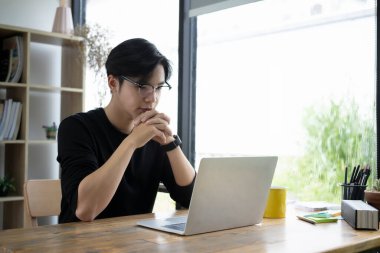 Düşünceli genç tasarımcı dizüstü bilgisayardan bilgi kontrol ediyor..