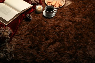 Kahve fincanı, kitap ve aroma mumu kahverengi halıda..