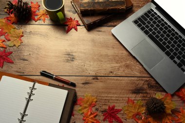 Dizüstü bilgisayar, kahve fincanı, defter ve sonbahar akçaağaç yaprakları ahşap masada..