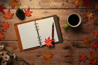 Yukarıda boş defter, kahve fincanı ve sonbahar akçaağaç yaprakları var..