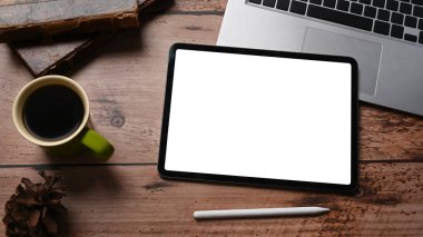 Dijital tablet, dizüstü bilgisayar, kahve fincanı ve ahşap masada çam kozalağı..