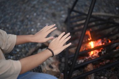 Ormanda kamp ateşinin yanında oturan genç bir kadın..