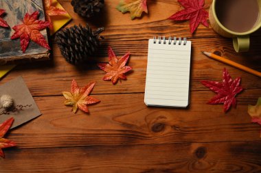 Boş not defteri, kahve fincanı, kozalak ve ahşap masada akçaağaç yaprakları..