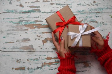 Yukarıda kırmızı kazaklı bir kadın Noel hediyelerini ahşap arka planda tutuyor..