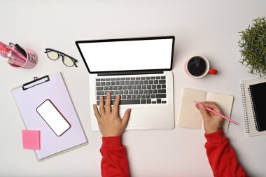 Diz üstü bilgisayarı kullanan ve not defterine not alan bir adam..