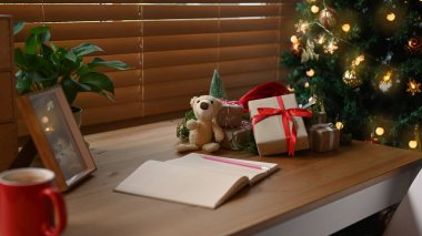 Not defteri, hediye kutuları ve oyuncak ayı oturma odasındaki Noel ağacının yanındaki tahta masada..