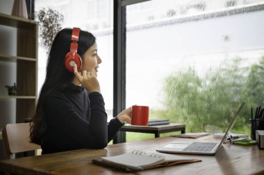 Genç Asyalı kadın kahve içmeyi ve kulaklıkla müzik dinlemeyi sever..