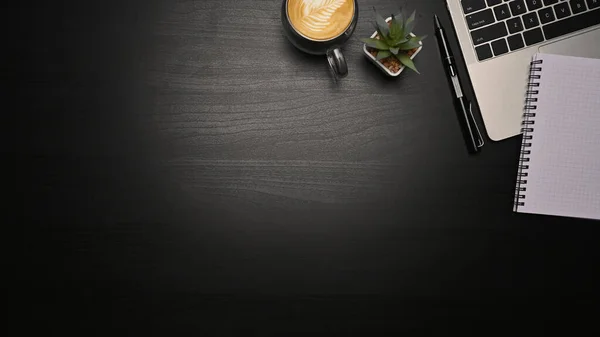 Top view laptop computer, notebooks and cup of coffee on black table. Copy space.