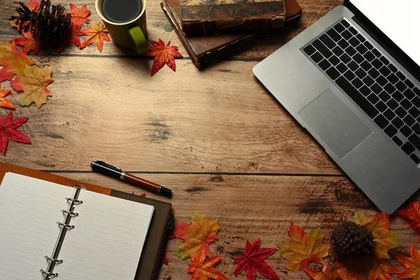 Dizüstü bilgisayar, kahve fincanı, defter ve sonbahar akçaağaç yaprakları ahşap masada..