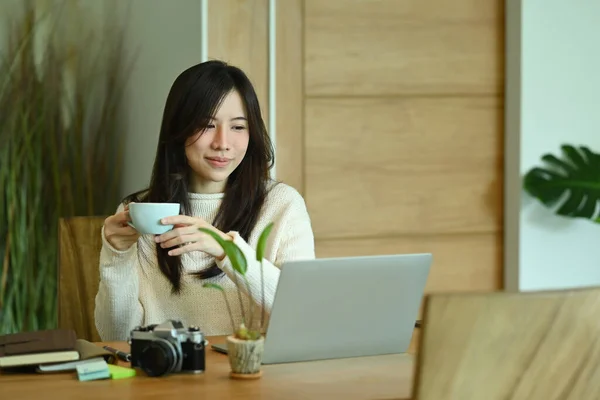 Χαμογελώντας Νεαρή Γυναίκα Πίνοντας Καφέ Και Διαβάζοντας Ειδήσεις Στον Φορητό — Φωτογραφία Αρχείου