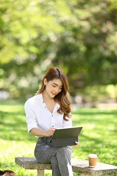 一个漂亮的年轻女子坐在公园的长椅上使用数码平板电脑的画像 — 图库照片