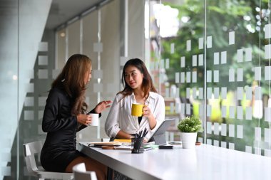 İki iş arkadaşı kahve molası veriyor ve ofiste birbirleriyle konuşuyorlar..