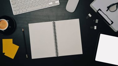 Boş defter, yapışkan notlar ve siyah masadaki dijital tablet.