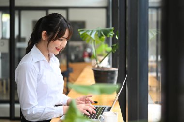 Güzel genç bayan ofis çalışanı parlak ofiste dizüstü bilgisayarla çalışıyor..