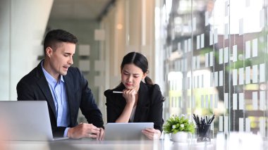 İş arkadaşları dijital tablet kullanıyor ve mali verileri birlikte tartışıyor.