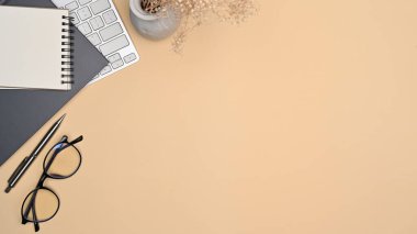 Bej arkaplanda gözlük, not defteri ve klavye.