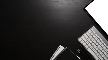 Görünümün üstünde, dijital tablet, klavye ve siyah masanın üzerindeki defter.