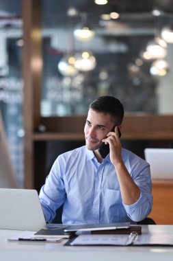 Genç girişimci dizüstü bilgisayarla çalışıyor ve cep telefonuyla konuşuyor..