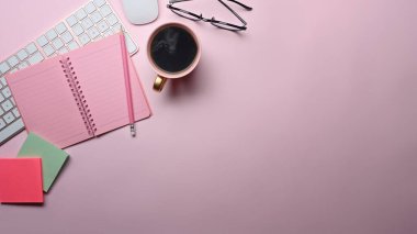 Üst görünüm defteri, kahve fincanı, yapışkan notlar ve pembe arka plandaki gözlükler..
