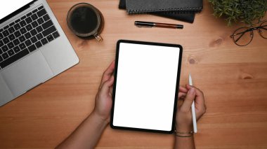 Tepedeki adam elinde boş ekranlı dijital tablet ve tahta masa üzerinde stil kalem tutuyor..